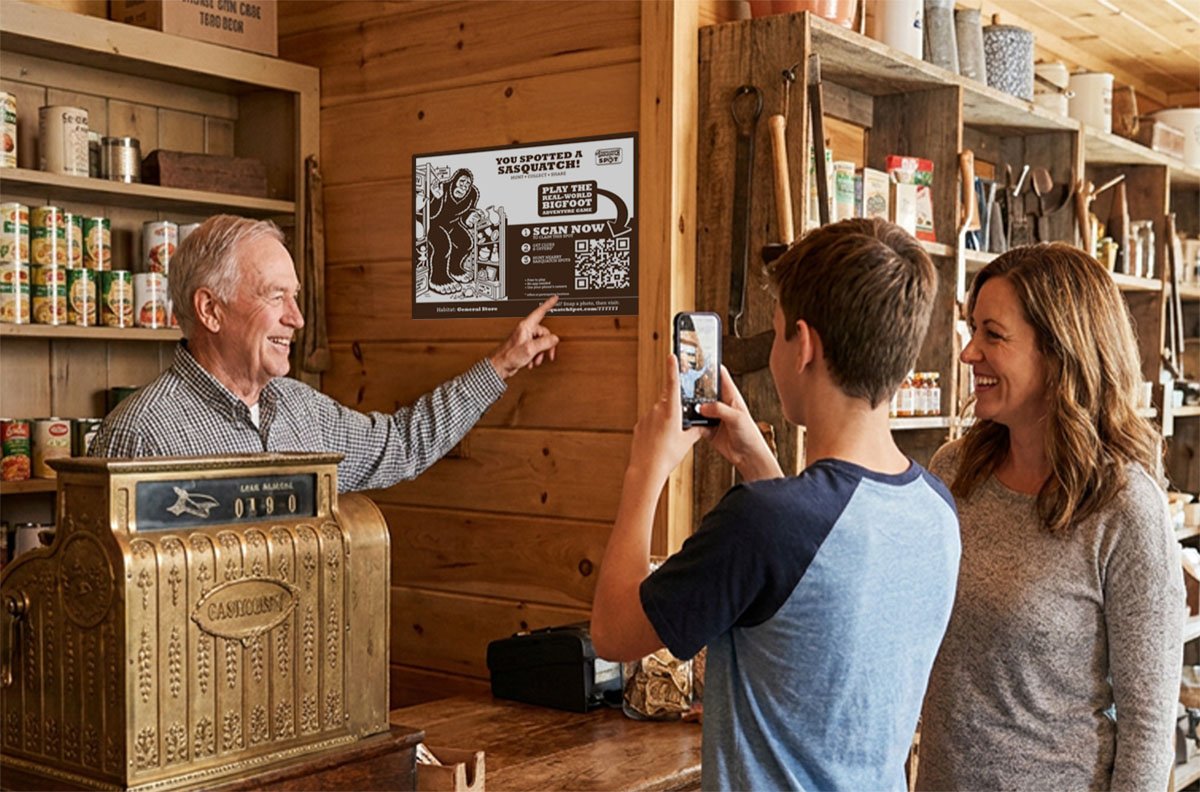 A boy scans a Sasquatch Spot sign on the wall of a general store while the shopkeeper points it out and his mom watches